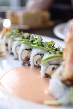 Delicious close-up of sushi roll topped with avocado and microgreens, served with sauce.