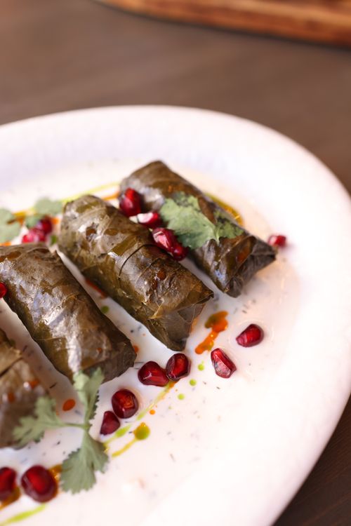 Free Dolma grape leaves with pomegranate seeds garnished with herbs on a white plate. Stock Photo