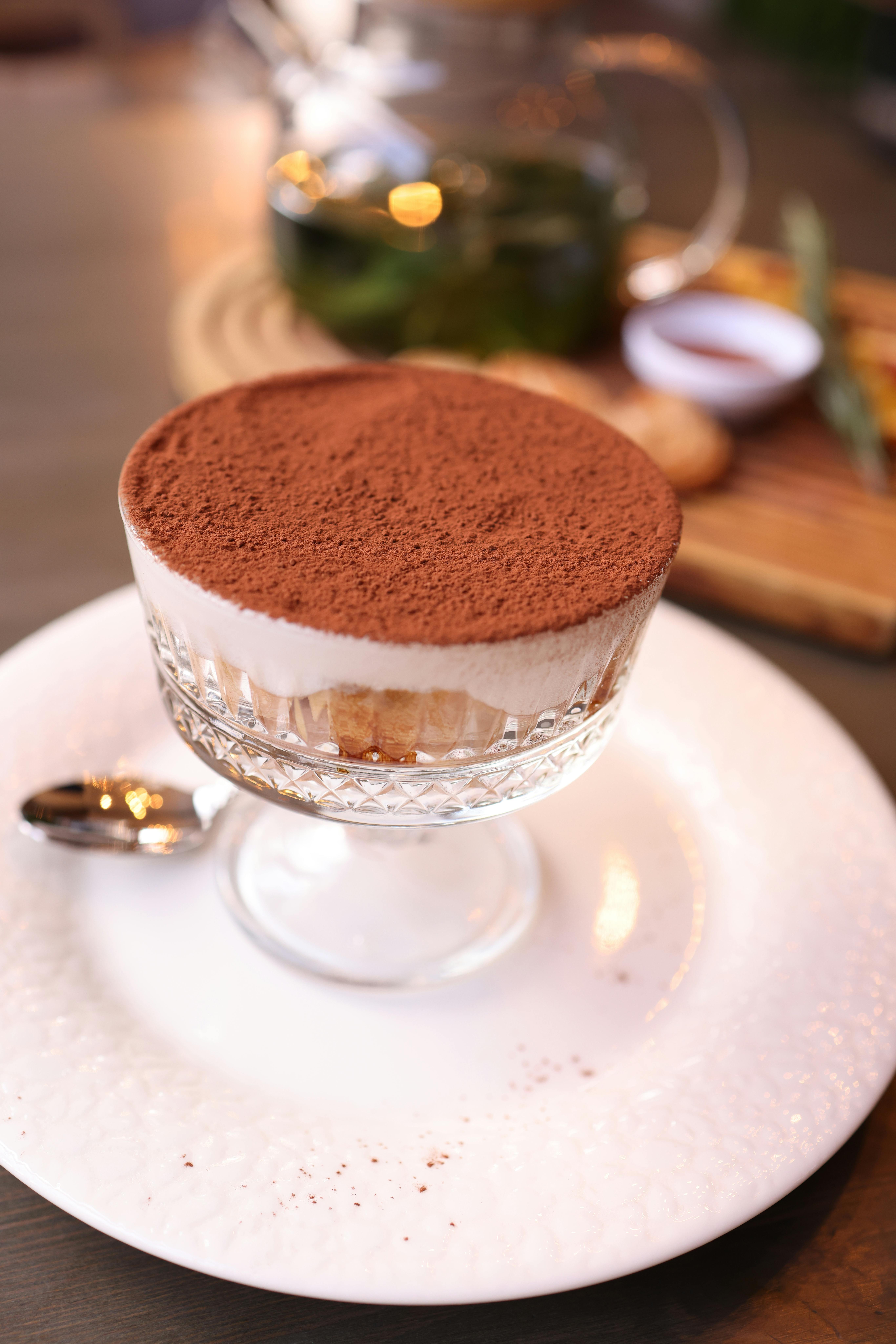 A delicious tiramisu in a glass cup, elegantly served with a spoon on a white plate.