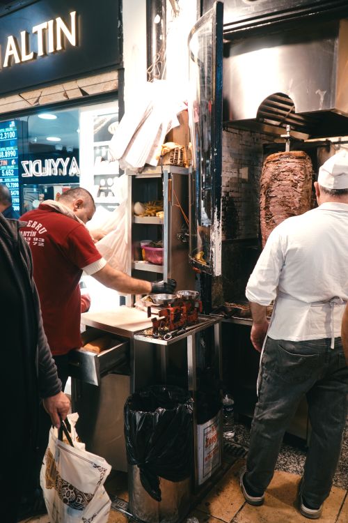 Free Street vendor preparing doner kebab in a bustling market. Authentic fast food experience with meat on spit. Stock Photo