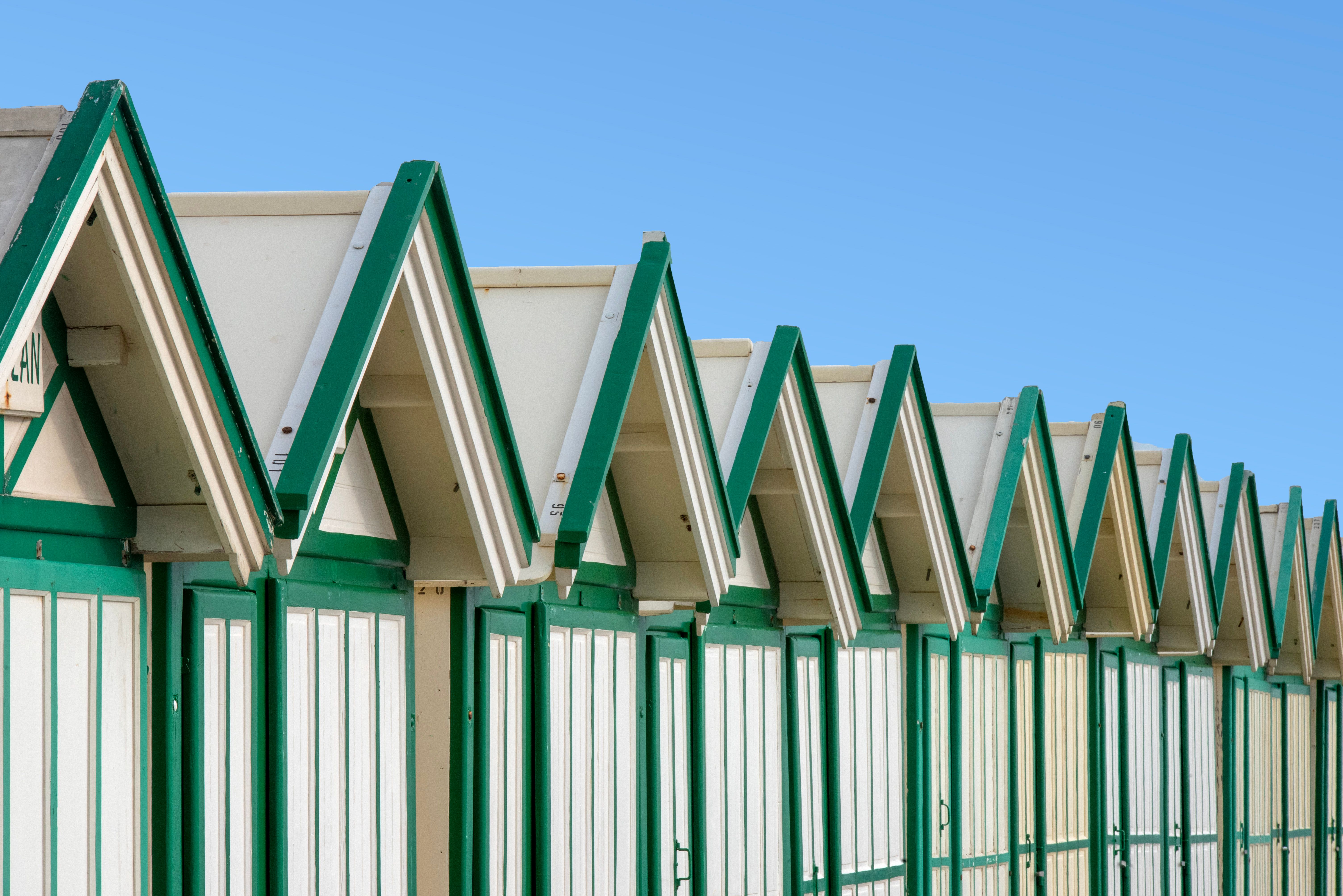 A row of vibrant green and white beach huts under a clear blue sky in Cayeux-sur-Mer, France.
