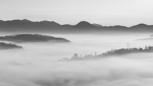 Tranquil black and white landscape featuring misty valleys and layered mountain silhouettes.