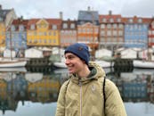 一名年轻人穿着外套，在哥本哈根的新港微笑着，身后是色彩缤纷的建筑