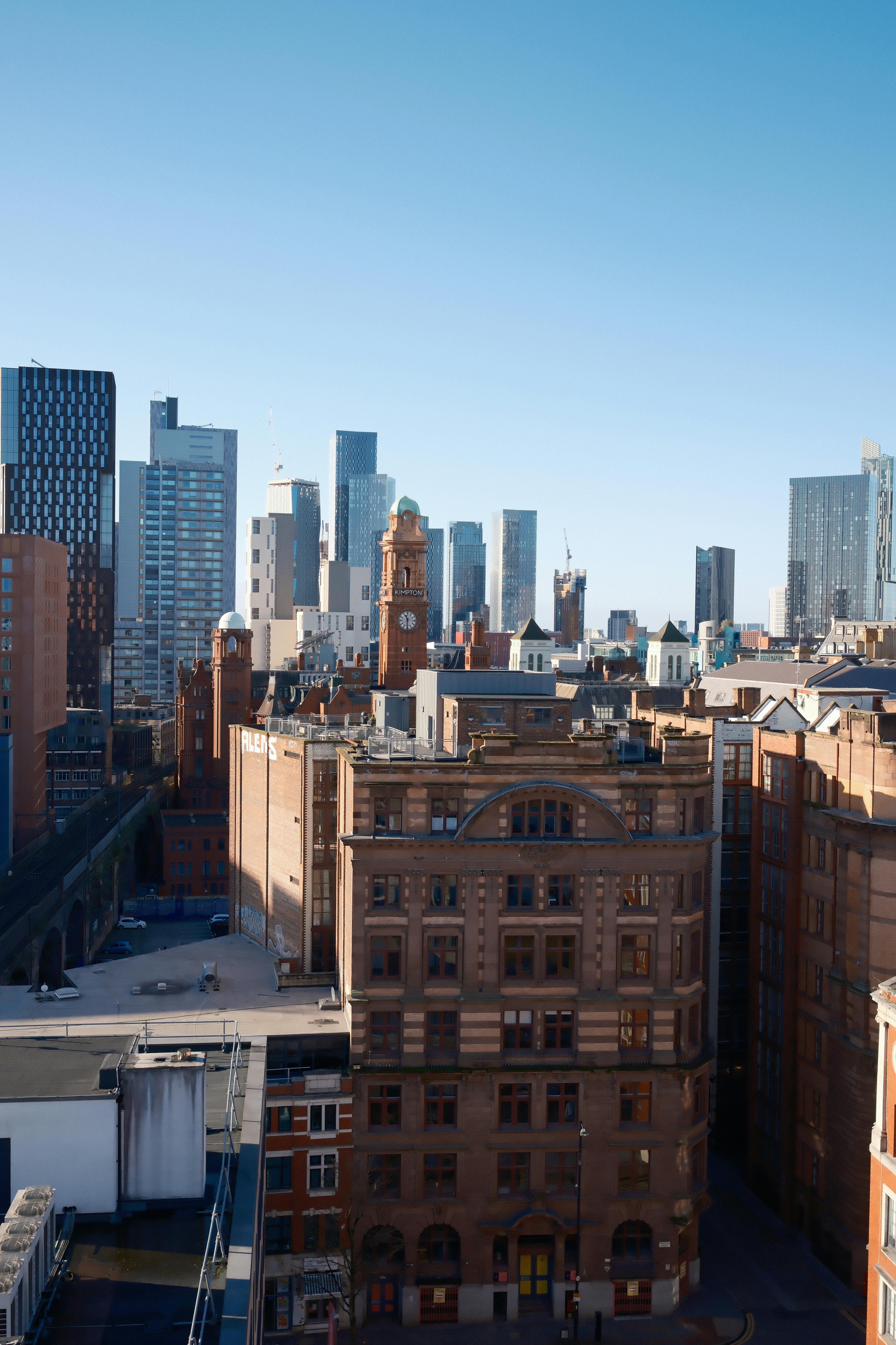 从城市天际线鸟瞰，现代高层建筑群中矗立着一座历史悠久的砖砌钟楼