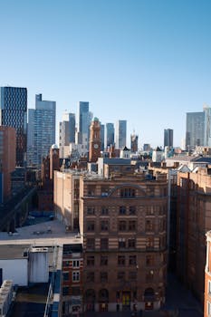 从城市天际线鸟瞰，现代高层建筑群中矗立着一座历史悠久的砖砌钟楼