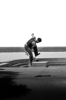 Skateboarder performs tricks in a skatepark with the ocean in the background.