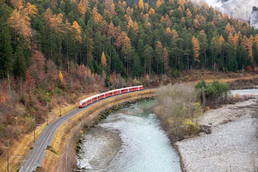 A red train traverses a picturesque autumn landscape in Safiental, Switzerland.