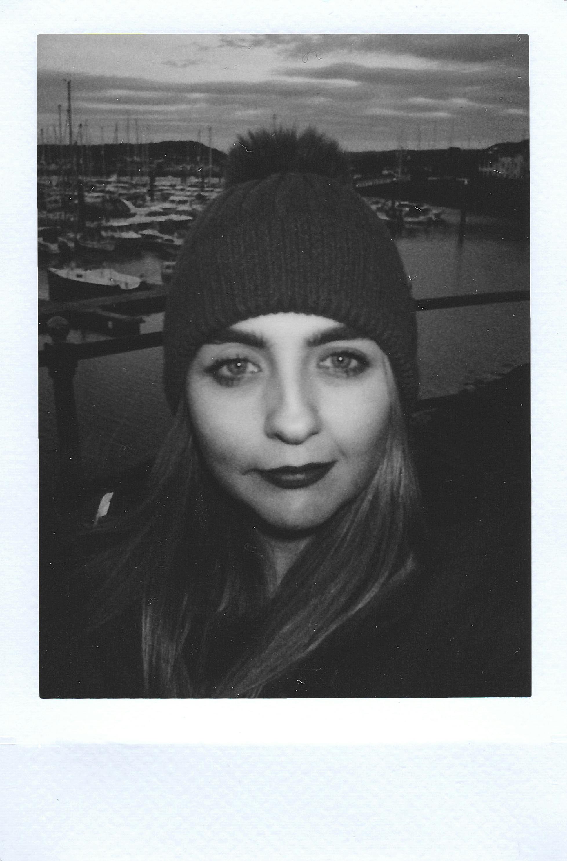Stylish woman in monochrome, wearing a beanie, by a marina backdrop.