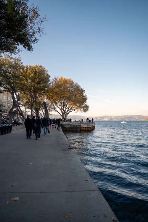 Free Peaceful autumn stroll along a waterfront with people enjoying the view. Stock Photo