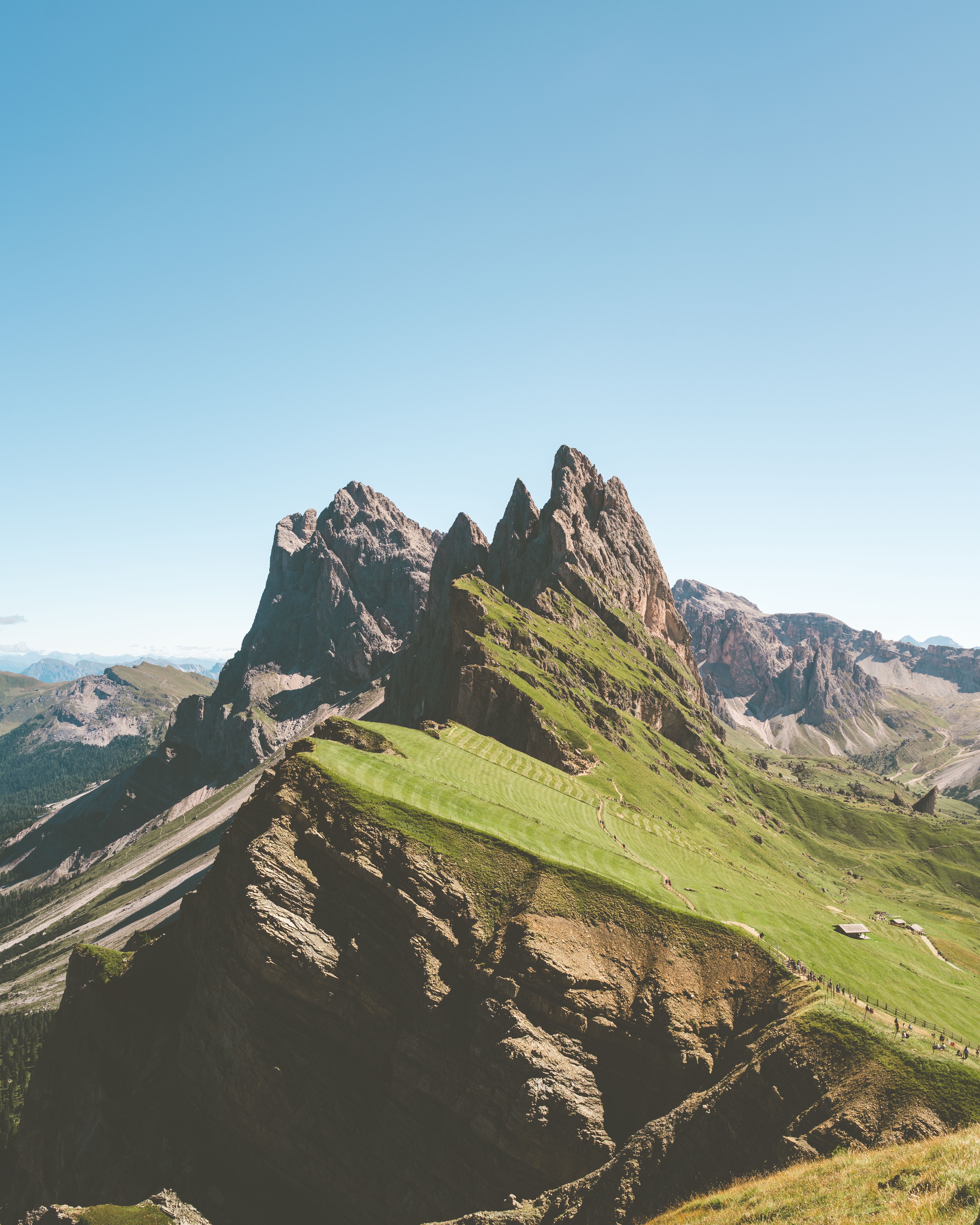 Majestic Seceda mountain peaks in the Italian Dolomites, showcasing rugged terrain and lush greenery under a clear blue sky.