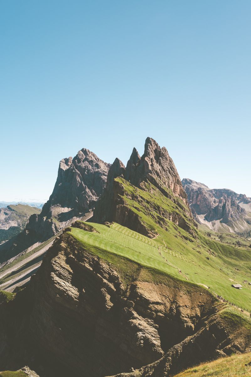 Majestic Seceda mountain peaks in the Italian Dolomites, showcasing rugged terrain and lush greenery under a clear blue sky.