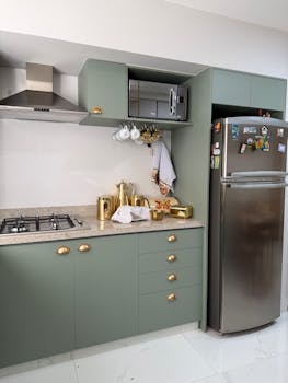 Contemporary kitchen with green cabinetry, stainless steel appliances, and gold accents.