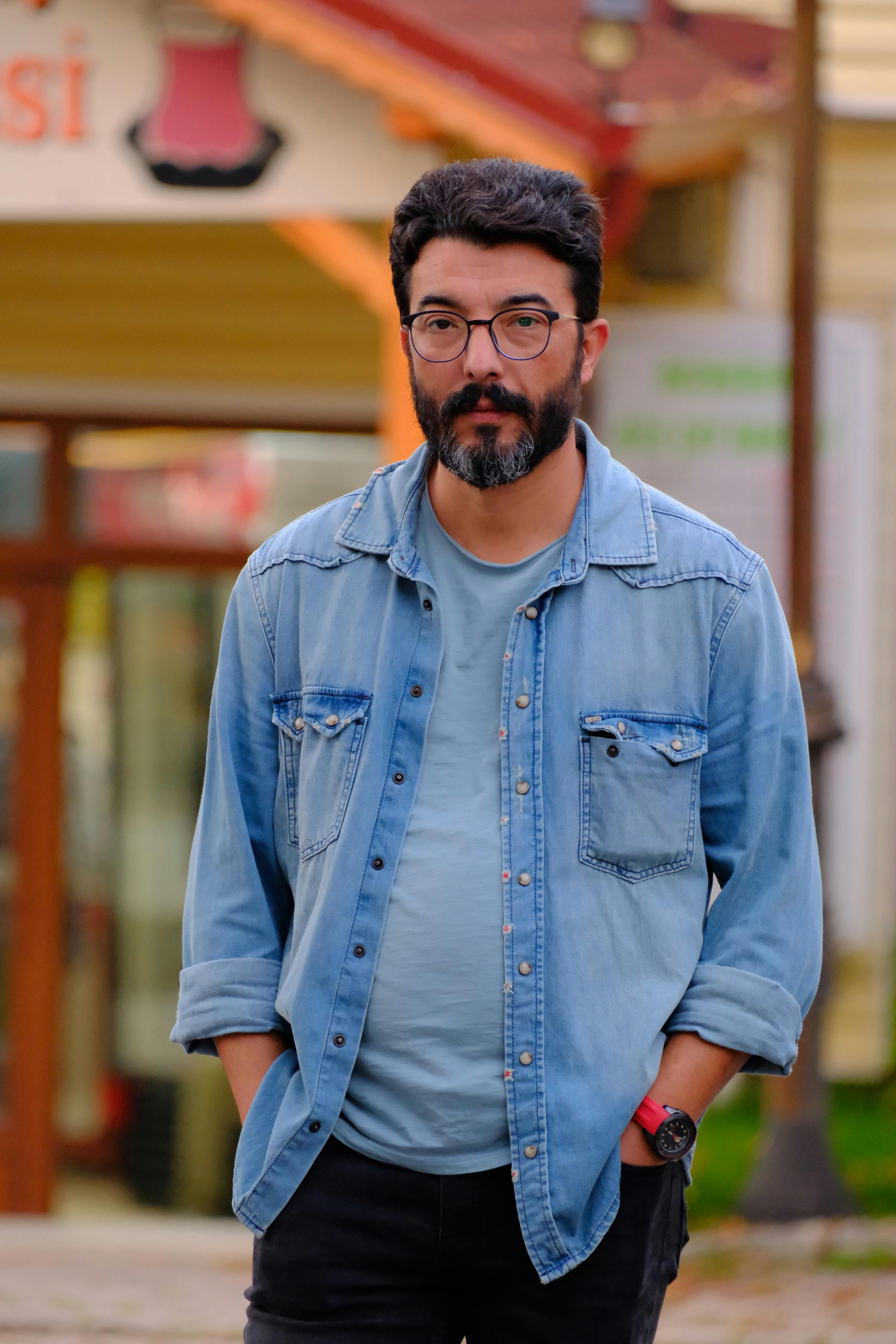 Man with beard wearing denim jacket standing outdoors. Casual and relaxed look.