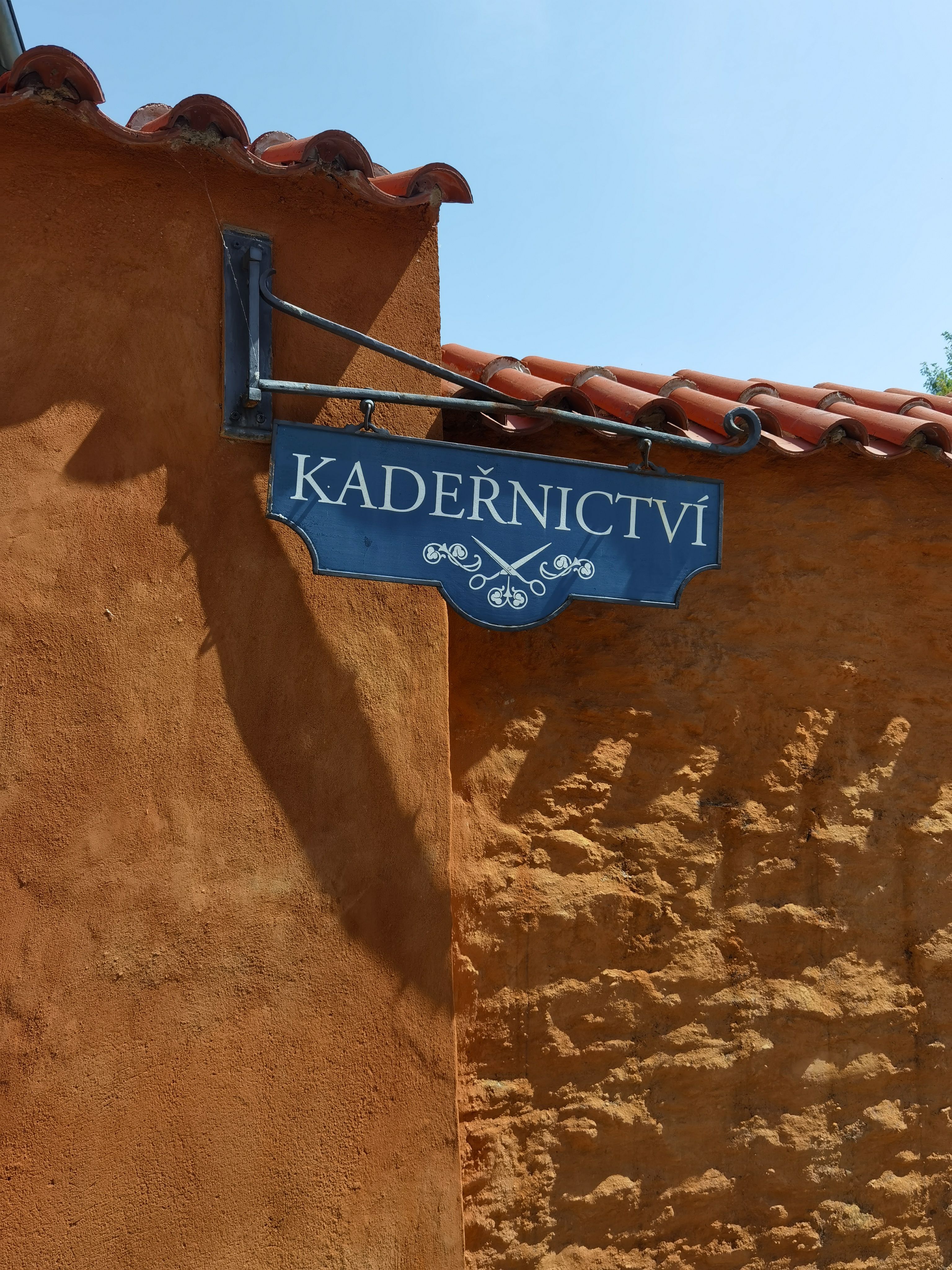 A vintage barber shop sign reading 'Kadeřnictví' against an old brick wall in Kutná Hora, Czech Republic.