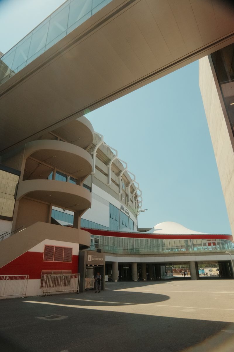 The red and white outer walls and curved stair towers of the Estadio Monumental in Buenos Aires under a clear sky.