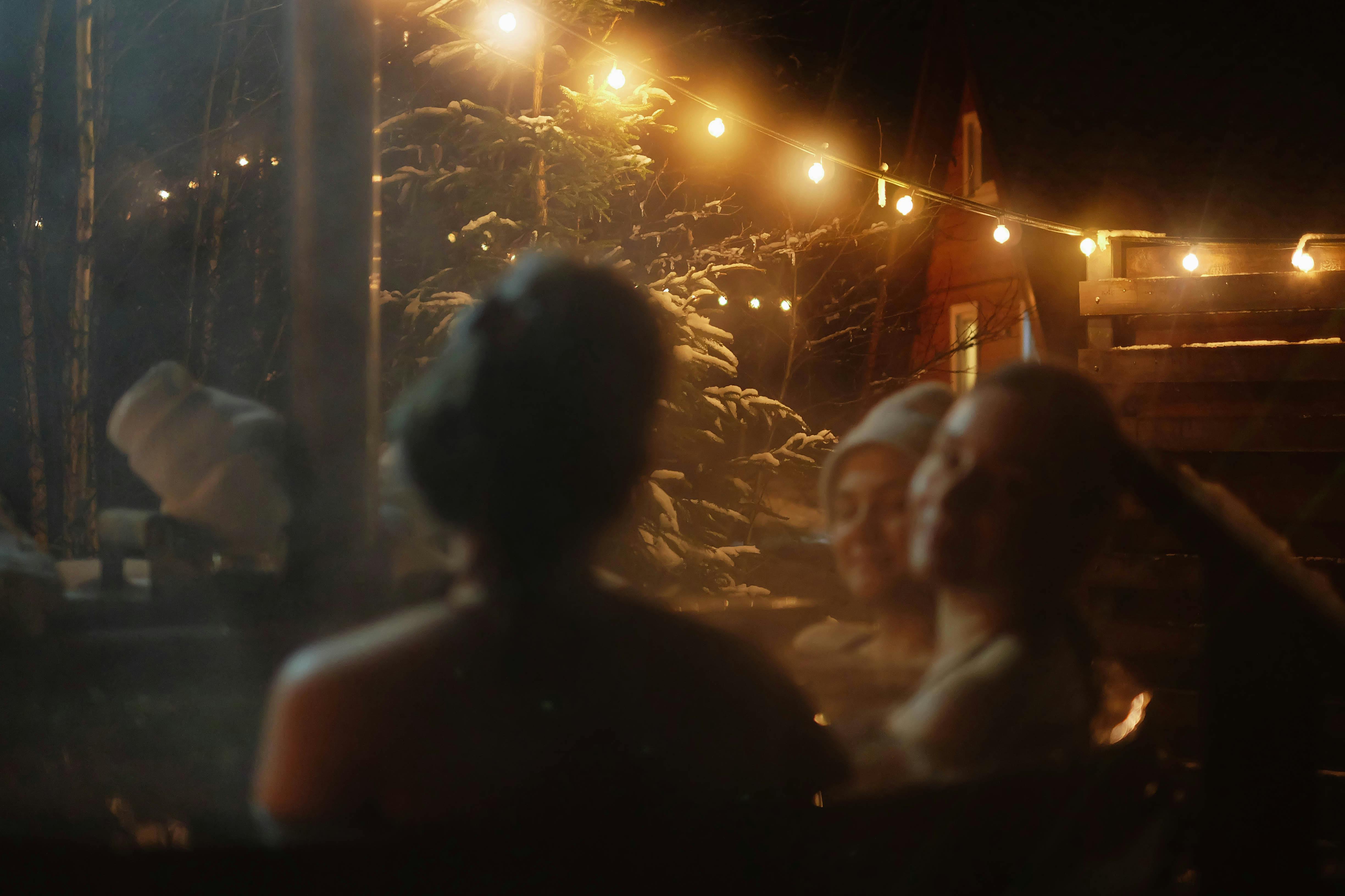 People enjoying a warm outdoor hot tub on a cozy winter evening with string lights and snow