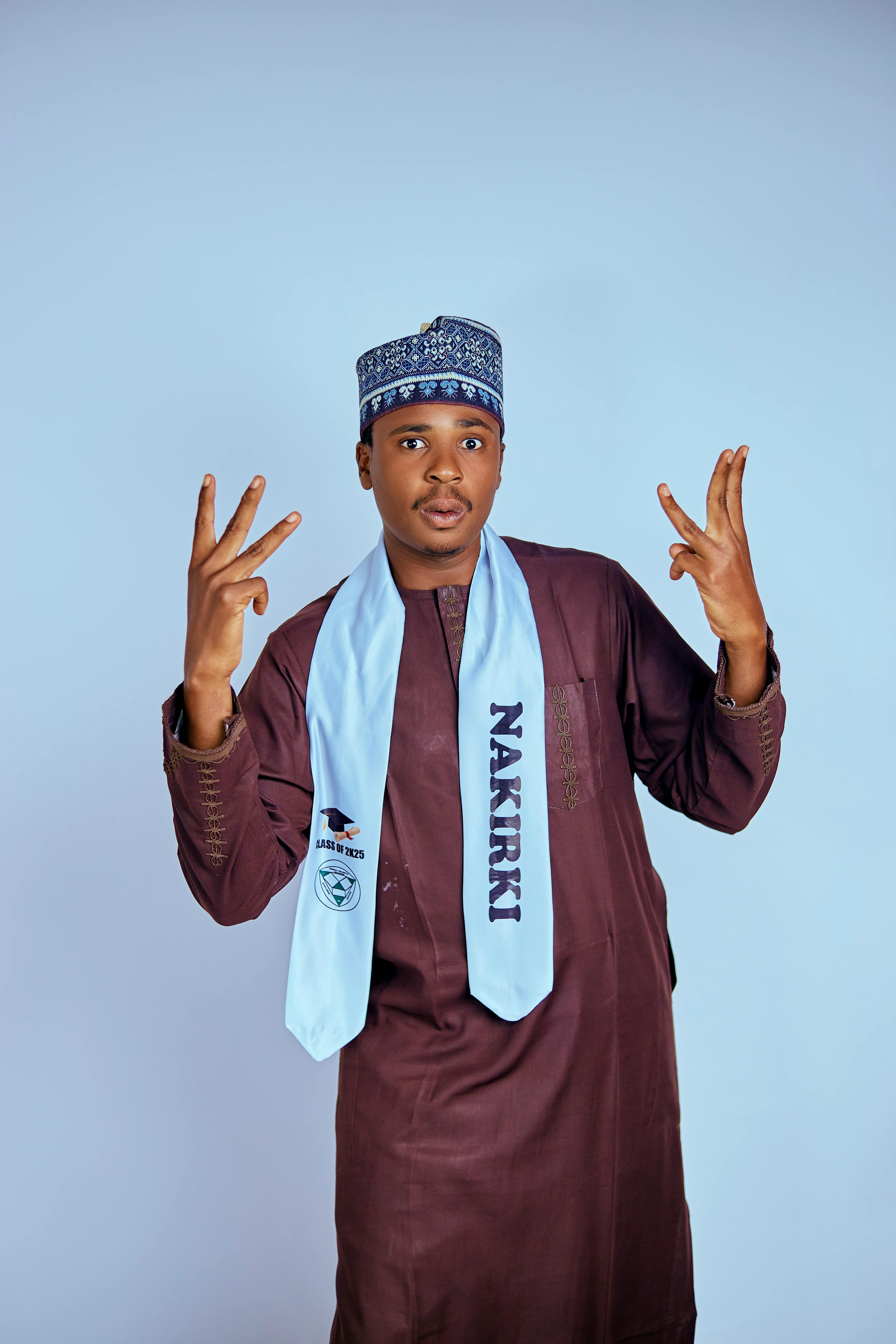 A young man in traditional attire celebrating with a graduation stole around his neck.