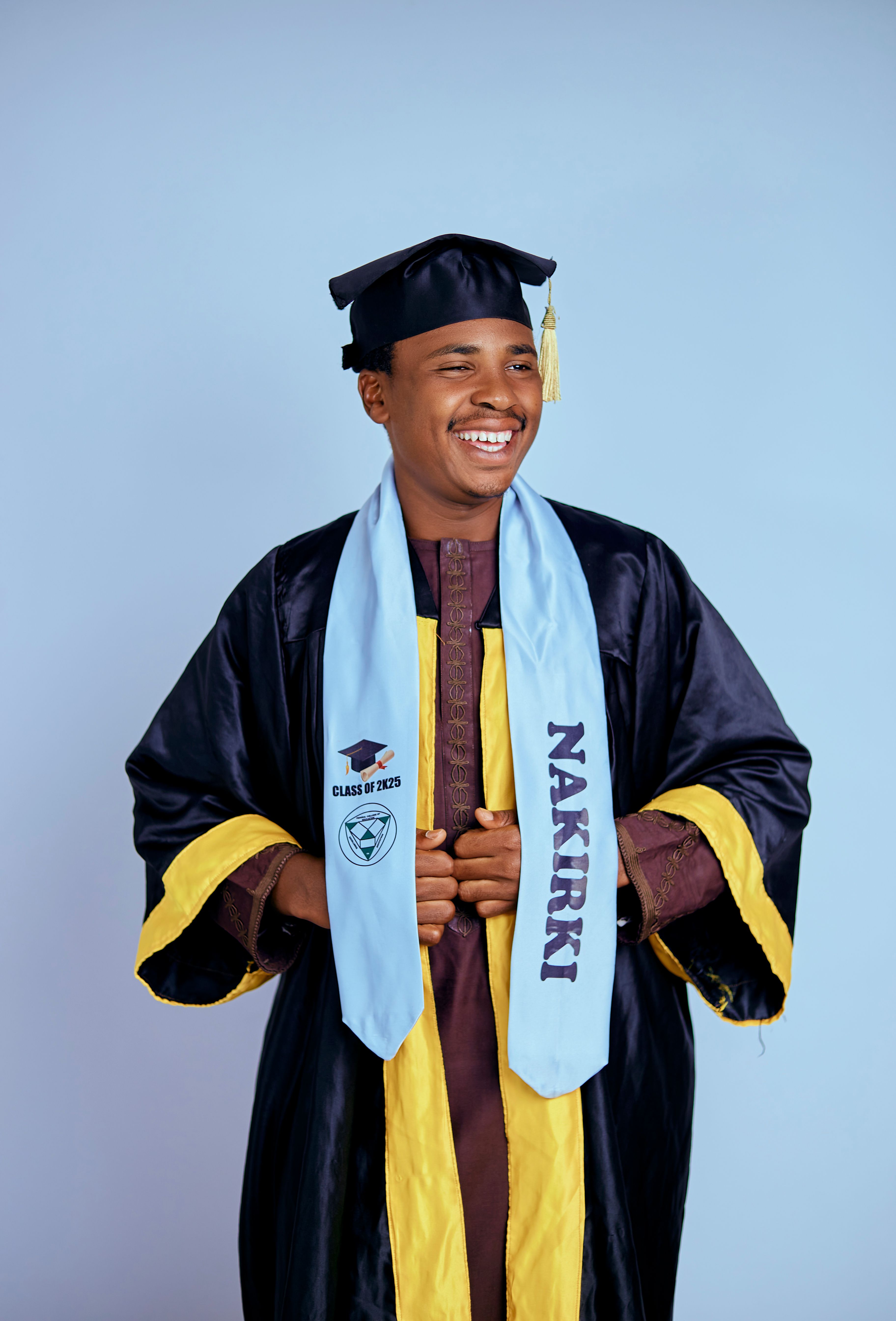 A happy graduate wearing cap and gown celebrates his achievement against a blue background.