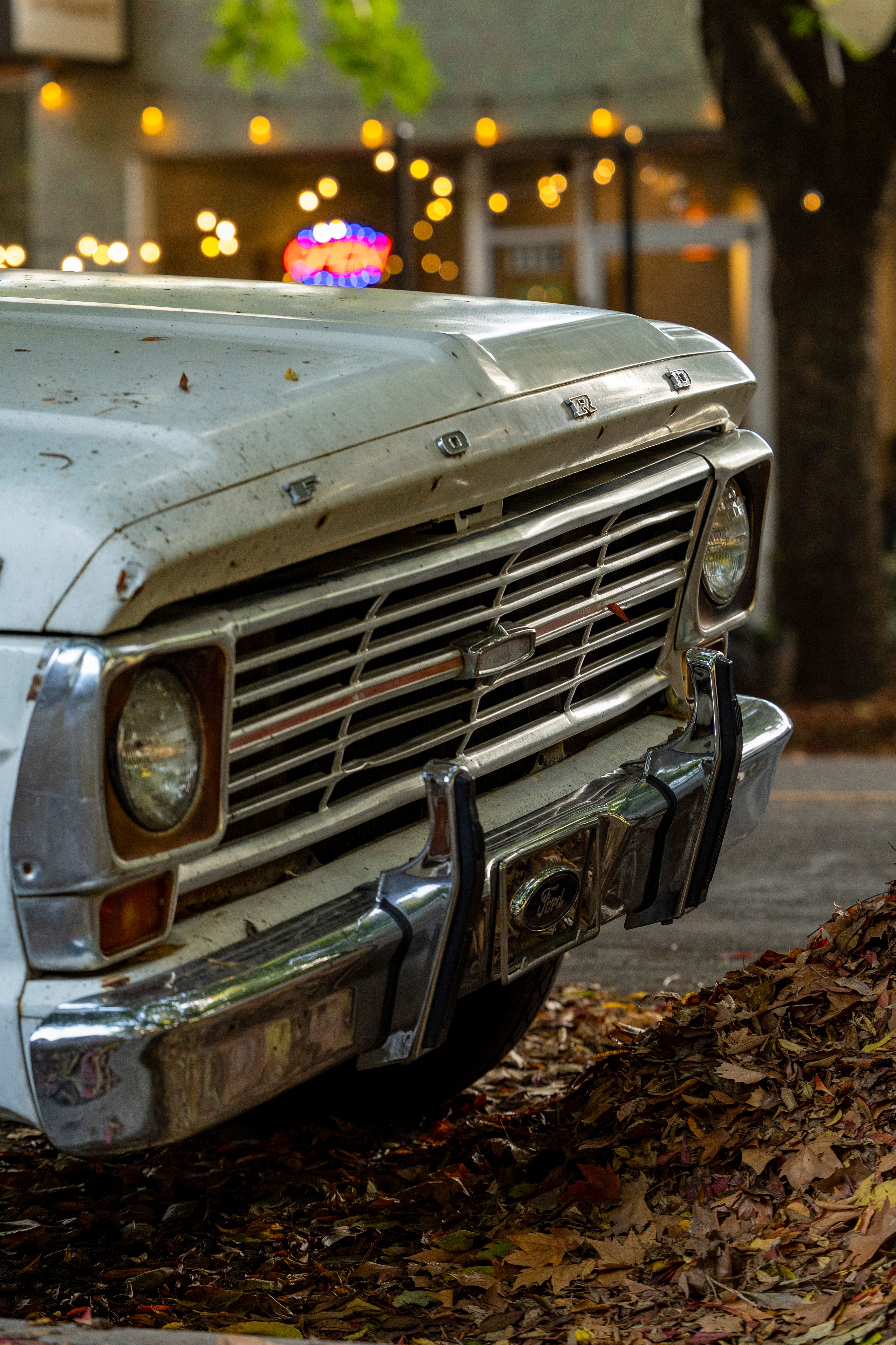 Close-up of a vintage truck's front in an urban setting with autumn leaves.