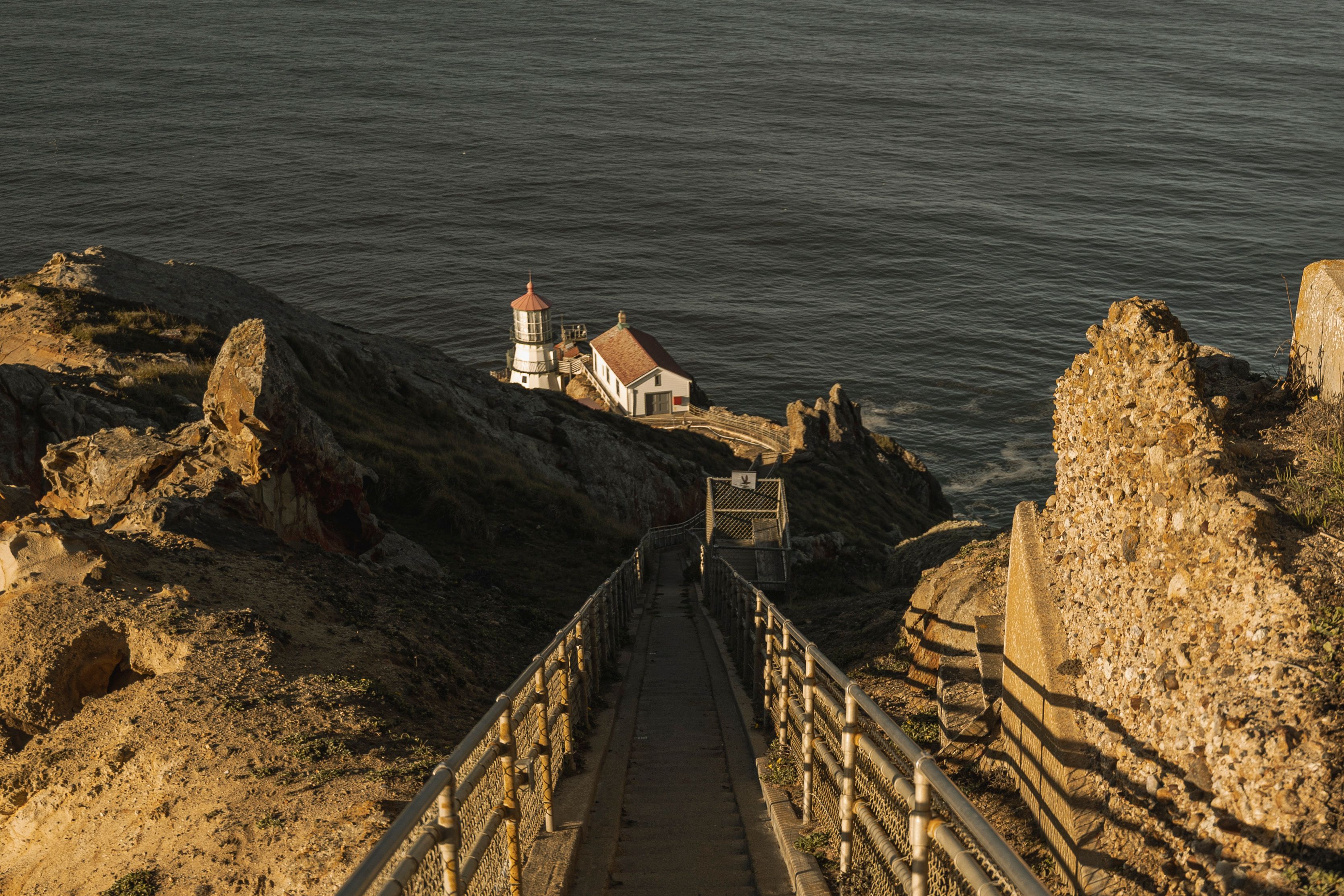 A captivating view of a lighthouse down a pathway with ocean cliffs during golden hour, evoking tranquility.