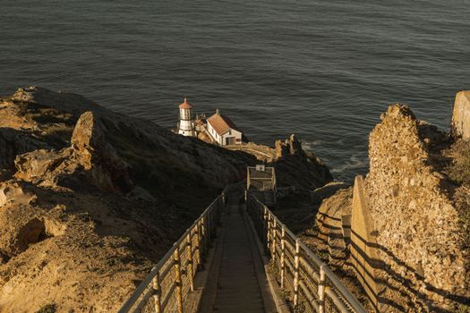 A captivating view of a lighthouse down a pathway with ocean cliffs during golden hour, evoking tranquility.