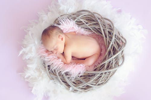 Free Baby Sleeping in a Basket and a Round Feather Surrounding the Basket Stock Photo