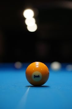 Close-up of an orange billiard ball with the number one on a blue pool table under dim lights.