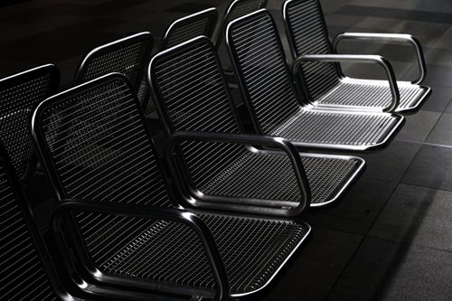 Free A row of empty metal seats in a dimly lit indoor location, creating a stark and modern atmosphere. Stock Photo