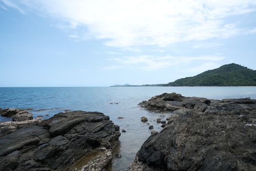 Peaceful rocky coastal scene showcasing a clear blue sea and distant green hills under a bright sky.
