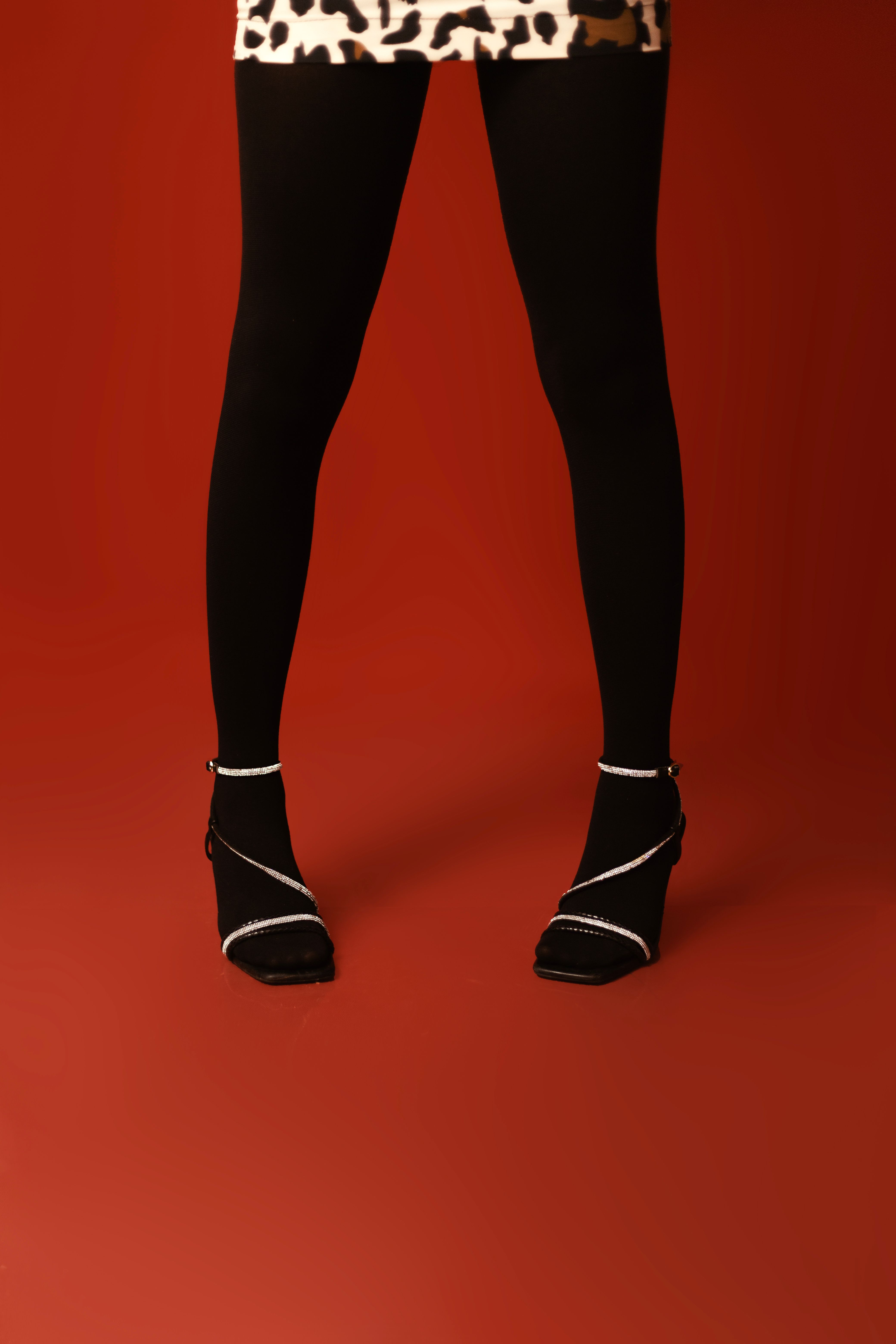 Fashionable black tights and heels against bold red backdrop, highlighting style.