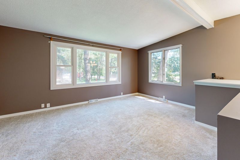 Large empty living room with neutral walls and carpet, natural light through windows.