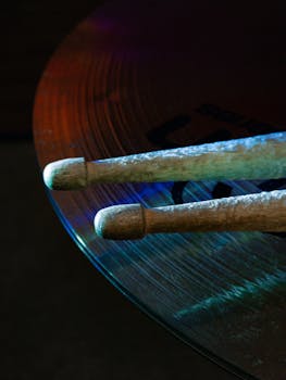 Artistic shot of drumsticks resting on a cymbal, highlighting jazz music elements with colorful lighting.
