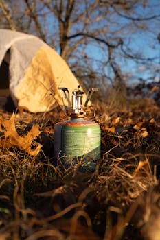 Portable camping stove set up amidst autumn leaves next to a tent outdoors.
