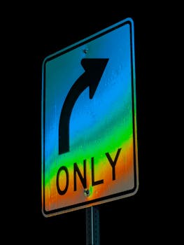Vibrant street sign illuminated at night with a reflective, multicolored glow.
