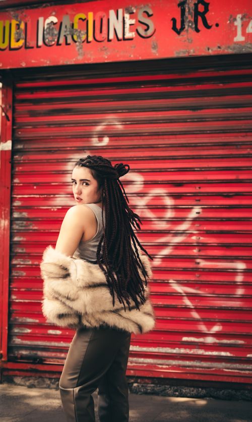 Free Fashionable woman with dreadlocks and fur coat posing in front of a red shutter. Urban and edgy vibe. Stock Photo