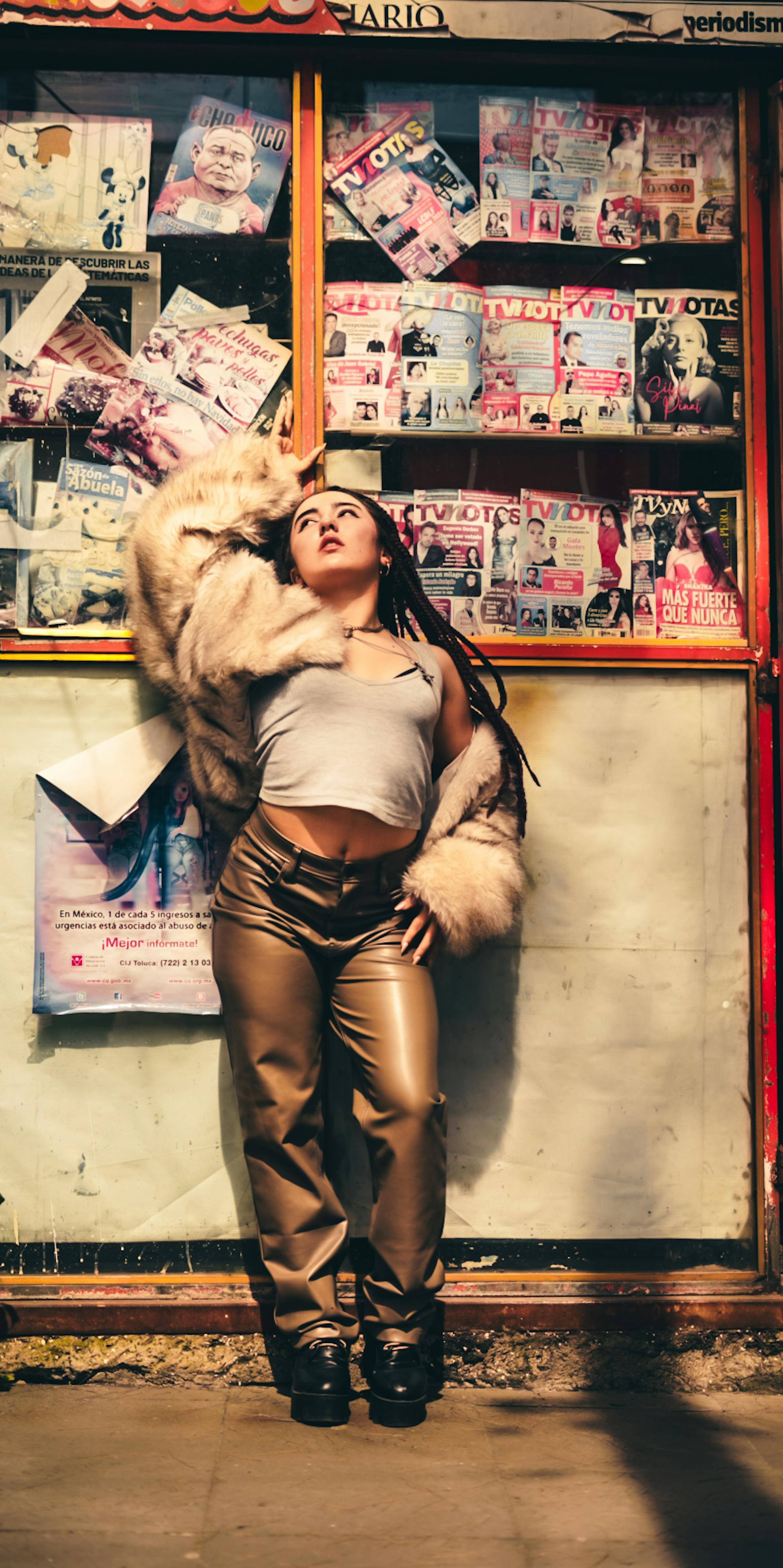 Fashionable woman in fur coat posed confidently against a vibrant magazine stand