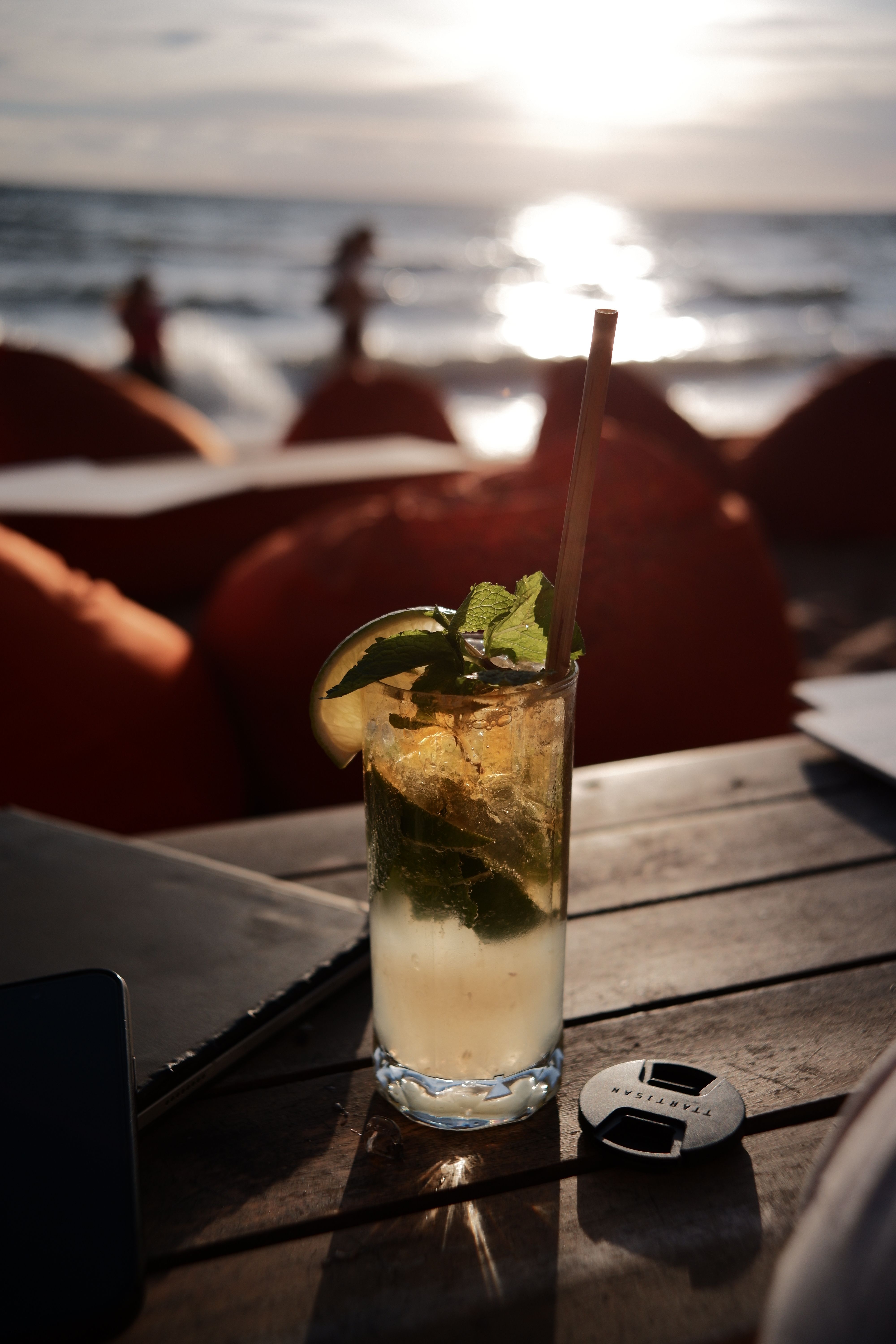 A vibrant mojito cocktail sits on a beach table at sunset with an ocean view, perfect for a tropical getaway.