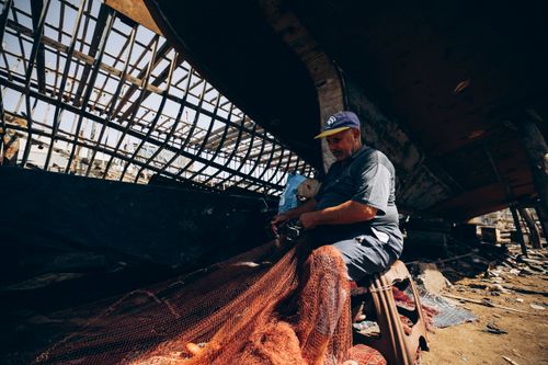 Free A fisherman in Damietta, Egypt, skillfully repairing nets under a boat, showcasing daily life by the shore. Stock Photo