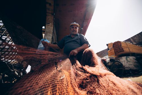 Free Fisherman repairing nets under the sun in Damietta, capturing traditional fishing culture. Stock Photo