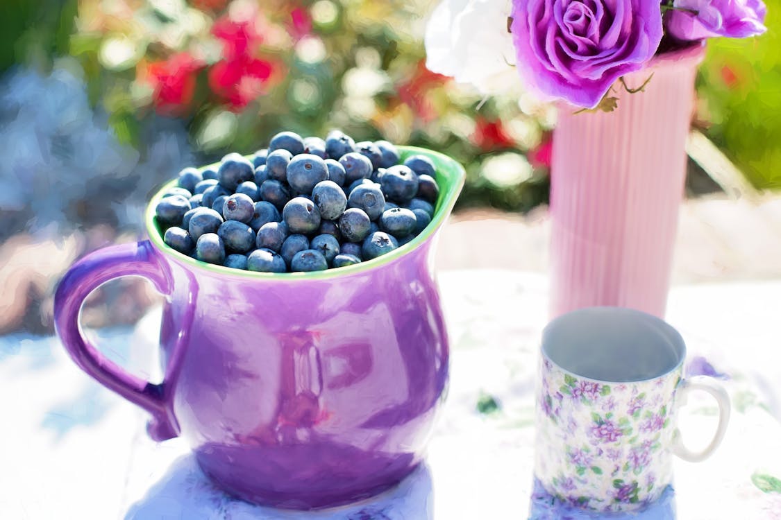 黑色漿果在白色和紫色花杯子旁邊的紫色容器
