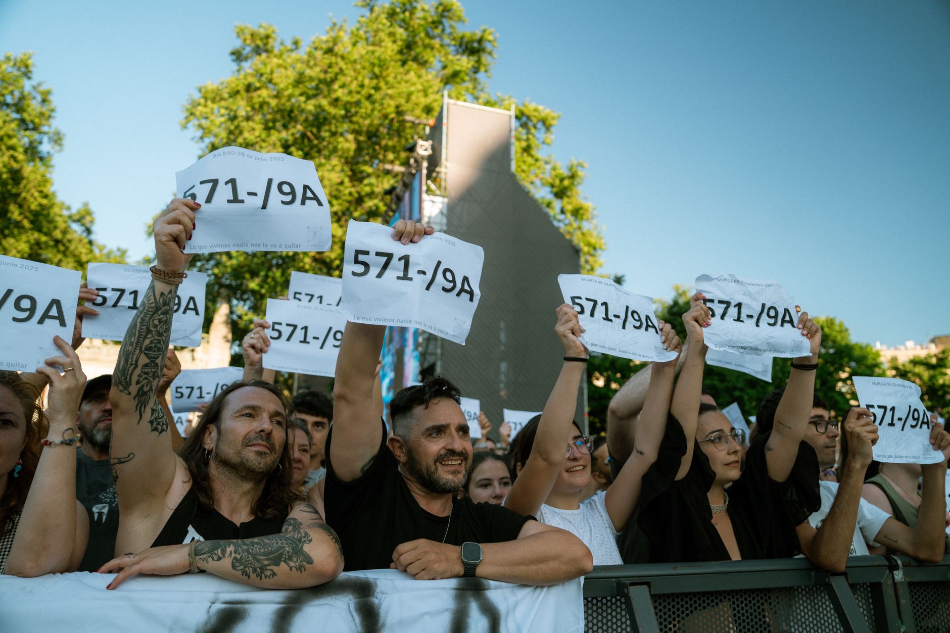 Diverse crowd holding numbered signs at an outdoor event in sunlight. Unity and expression.