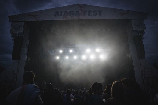 A misty night music festival scene with bright stage lights and a crowd of people.