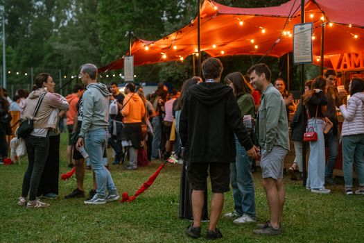 A lively outdoor festival with people socializing under a tent with string lights.