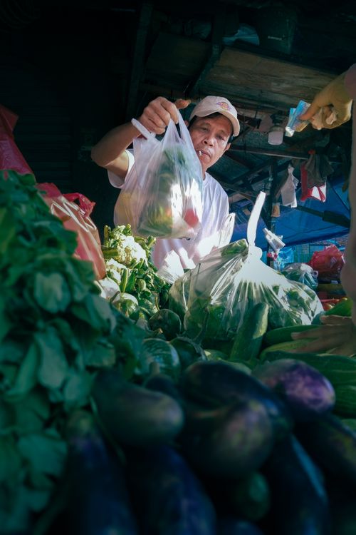 Free A vendor handing fresh vegetables to a customer in a bustling outdoor market. Stock Photo