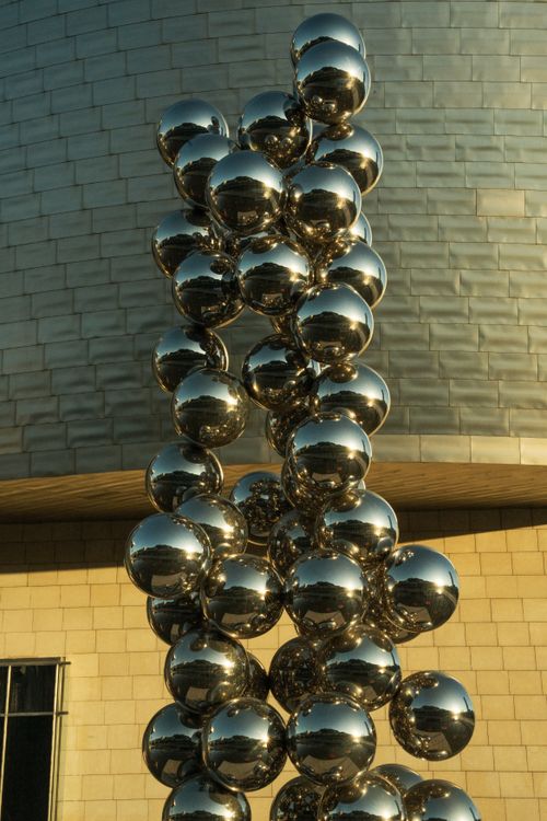 Free Close-up of a metallic reflective sculpture against modern architecture during day. Stock Photo