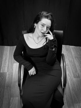 Black and white portrait of an elegant woman seated on a chair, looking confidently at the camera.