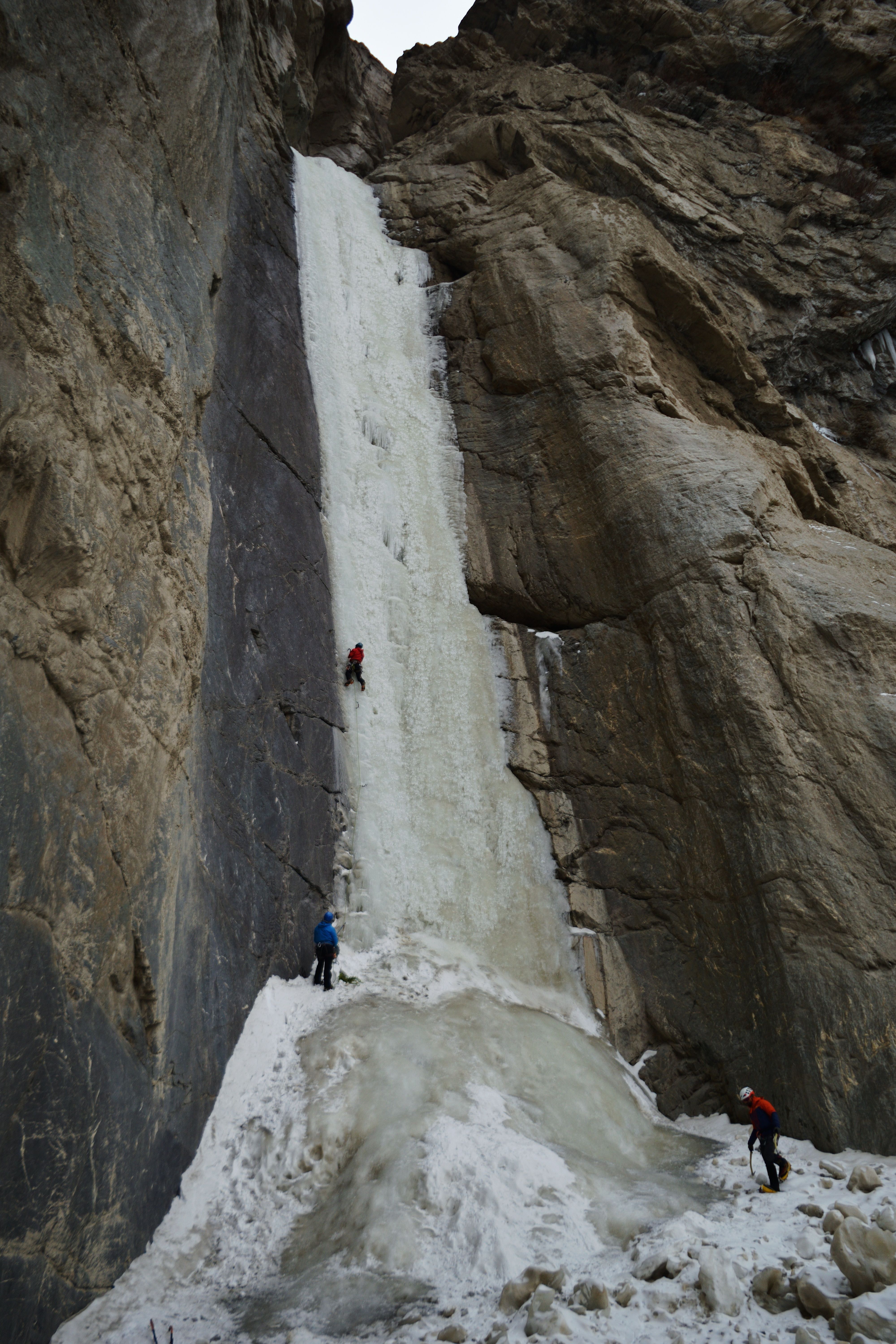 Thrilling ice climbers scaling a towering frozen waterfall in a dramatic winter landscape.