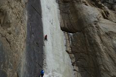 Thrilling ice climbers scaling a towering frozen waterfall in a dramatic winter landscape.