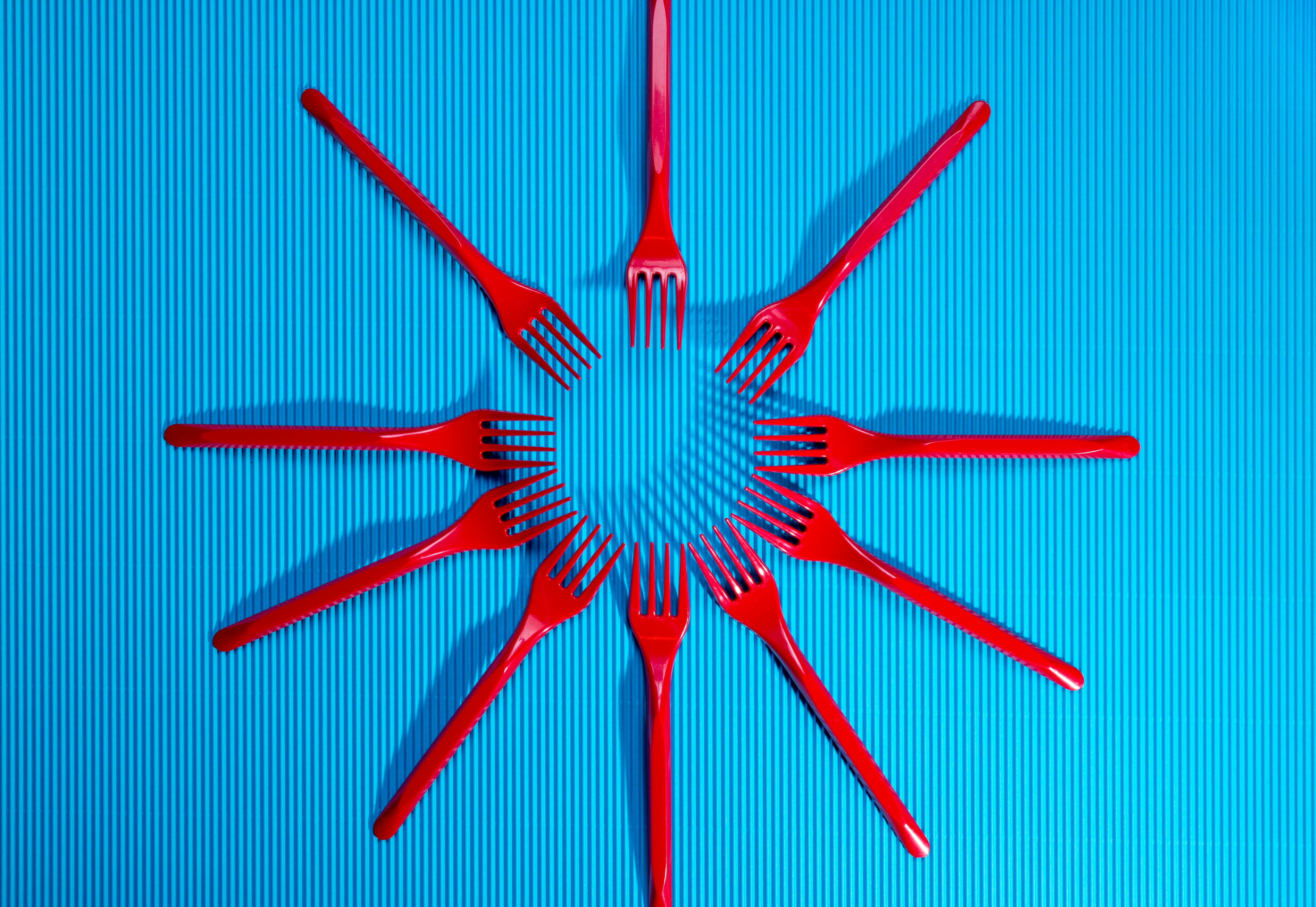 Free Creative arrangement of red plastic forks forming a sunburst on a blue corrugated background. Stock Photo