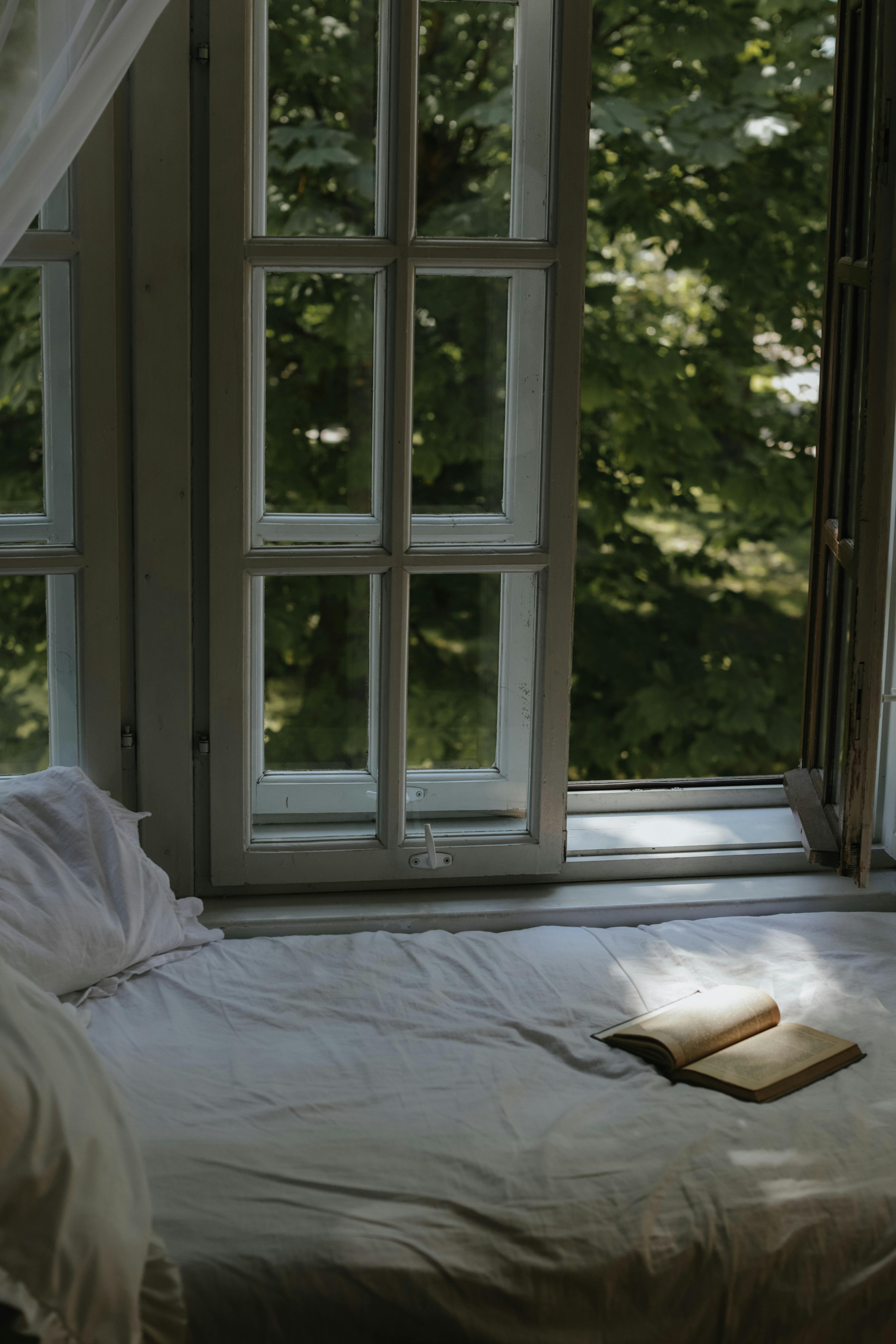 Free A serene bedroom featuring an open window and a book, inviting relaxation. Stock Photo